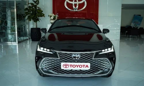 تویوتا آوالون هیبرید در نمای روبرو با لوگوی تویوتا در فضای نمایشگاهی