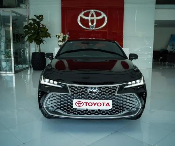 تویوتا آوالون هیبرید در نمای روبرو با لوگوی تویوتا در فضای نمایشگاهی