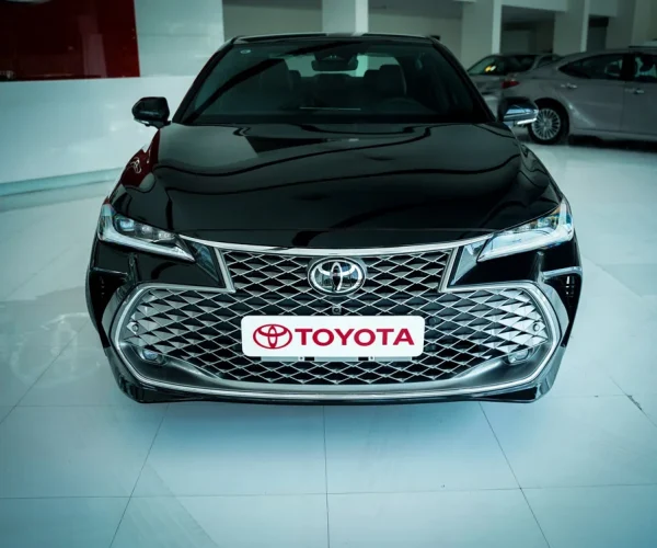 تویوتا آوالون هیبرید در نمای روبرو با لوگوی تویوتا در فضای نمایشگاهی